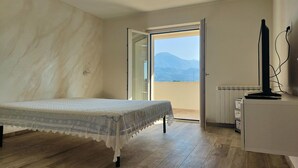A bedroom with a bed, a desk, and a view of mountains through an open door. - Holiday home for 5 Lido di Camaiore (Lido di Camaiore)