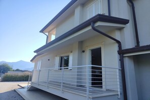A two-story building with a balcony, a window with shutters, and a visible door.