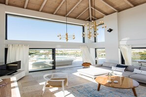 A spacious living room with a large TV, comfortable seating, and a view of the outdoors. - Seaview 4 bedroom Villa (Tersanas)
