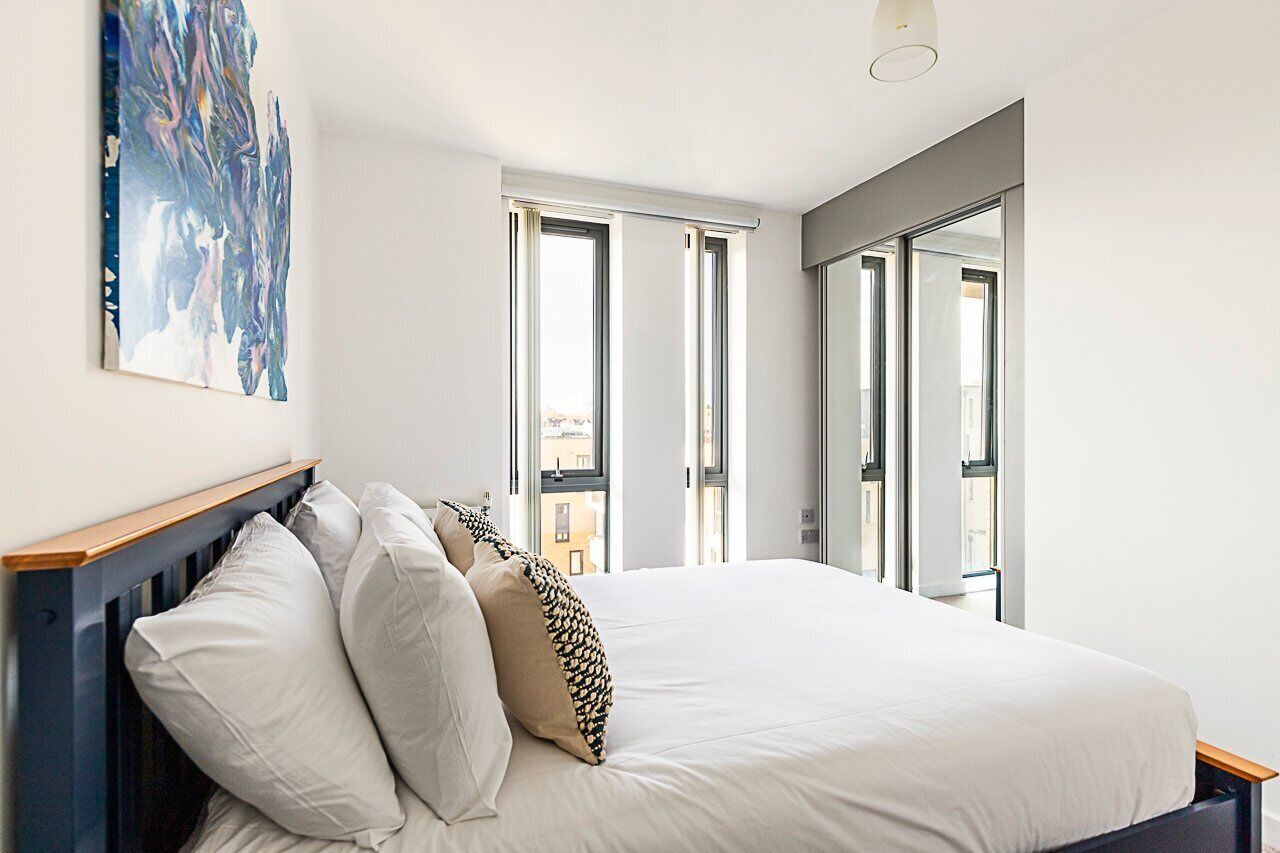 A bedroom with a large bed, multiple windows, and a painting on the wall.