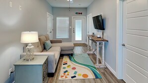 A modern living room with a sofa, a coffee table, a TV on a stand, and a patterned rug. - Port A Retreat w/ Rooftop Balcony + Community Pool! (Port Aransas)