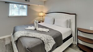 A neatly made bed with a grey quilt, white pillows, and a fluffy white throw.
