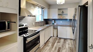 A modern kitchen with white cabinets, a stainless steel refrigerator, a built-in oven, and a microwave.