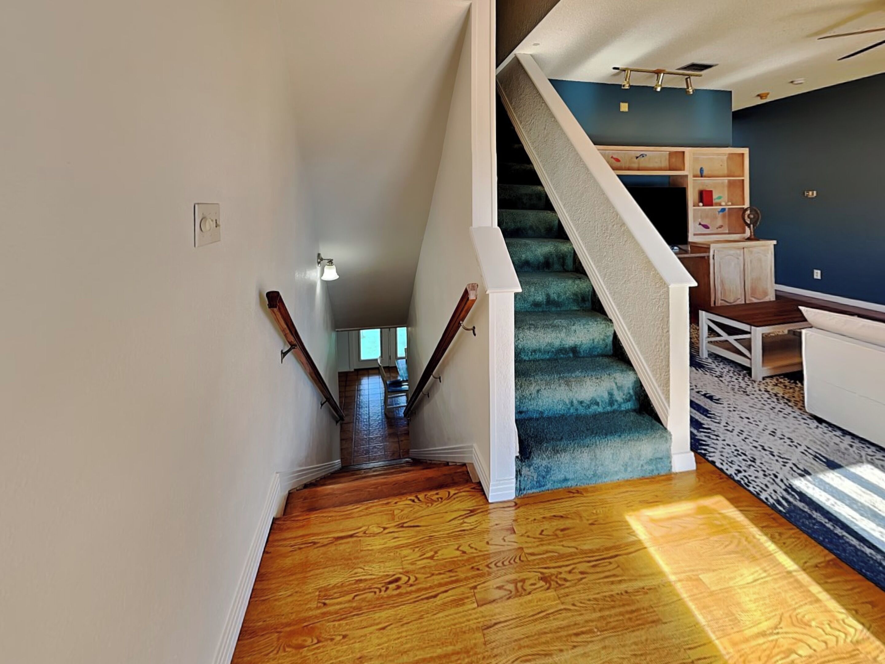 A staircase with wooden steps and a blue carpet, leading to a room with a white sofa and a patterned rug.