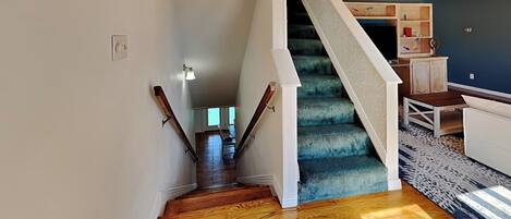 A staircase with wooden steps and a blue carpet, leading to a room with a white sofa and a patterned rug.