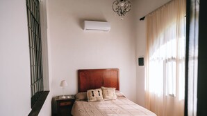 Een slaapkamer met een houten hoofdbord, een bed met beige beddengoed, een nachtkastje met een lamp en een airconditioning op de muur.
