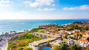 A coastal town with a view of the sea, featuring residential buildings, a swimming pool, and a road leading to the beach.