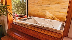 A modern bathroom with a large bathtub, wooden flooring, and a brick wall.