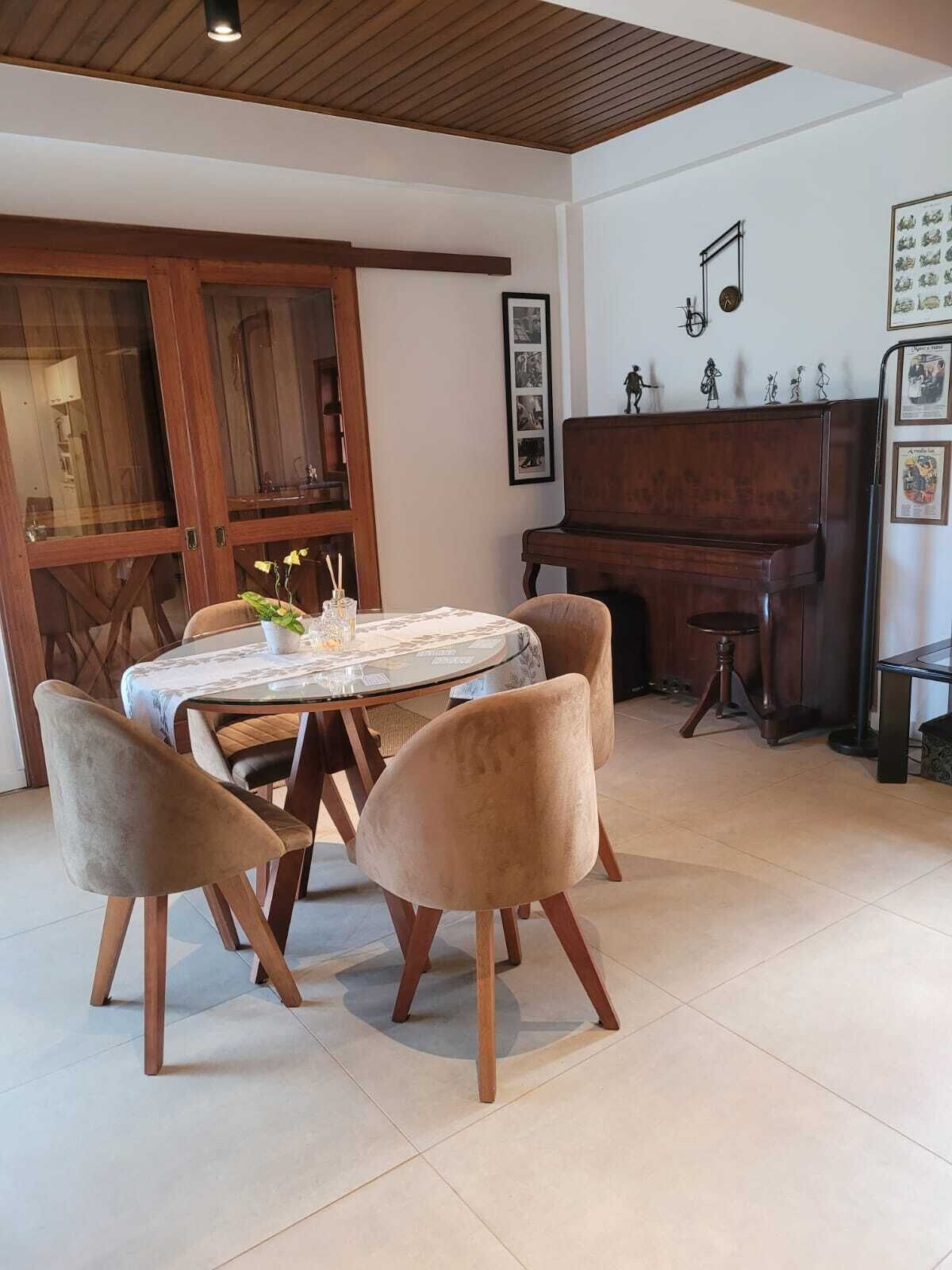 Un comedor con una mesa redonda, cuatro sillas, un piano y un reloj de pared.