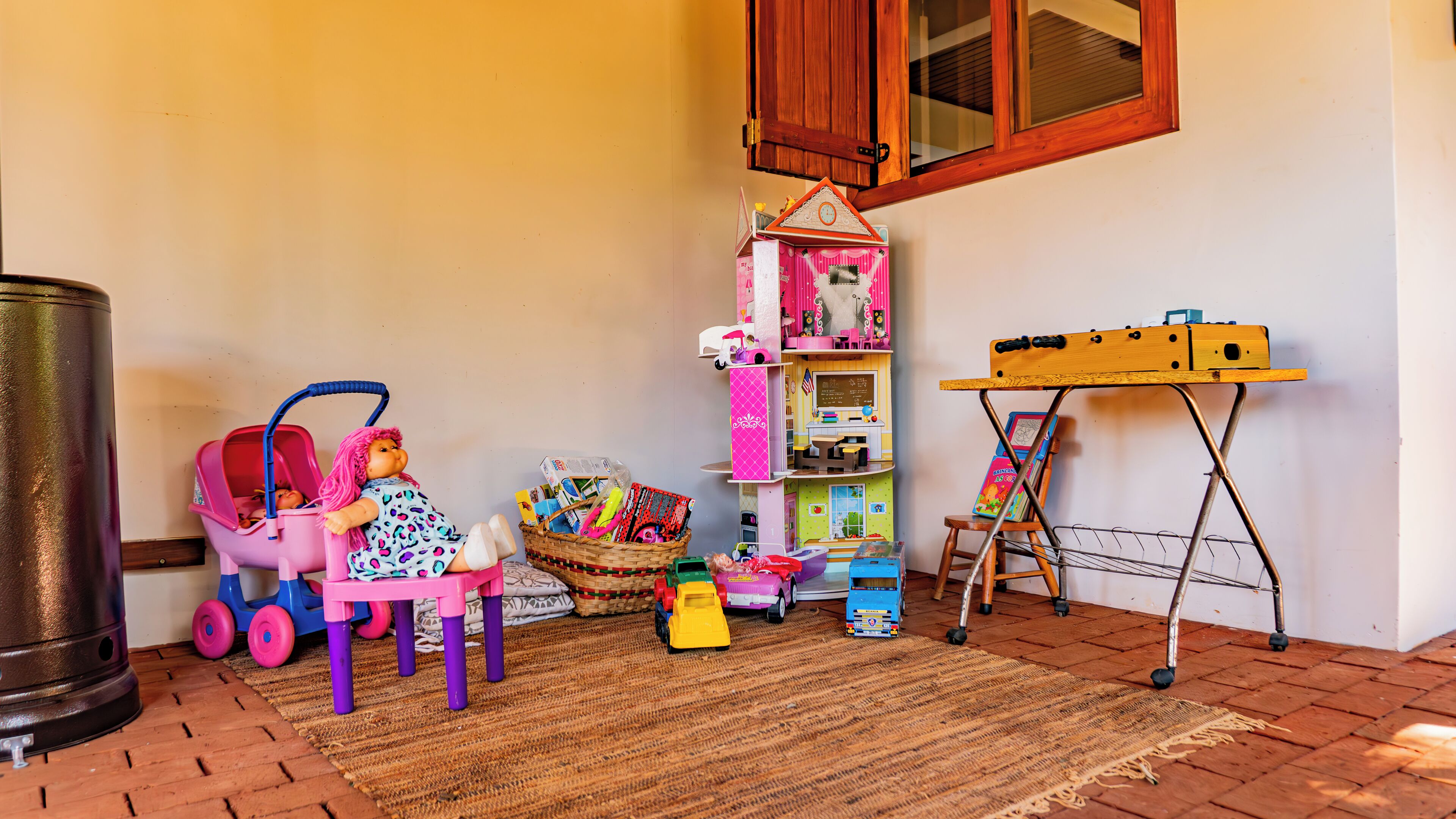 A playroom with a doll in a pink stroller, a toy car, and a toy kitchen set.