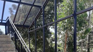 A staircase with glass railings leading to a covered area with a view of trees. - Invernada Blessmann  (Vespasiano Corrêa)