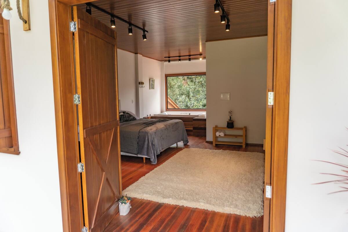 A bedroom with a bed, a window, a wooden floor, and a door.
