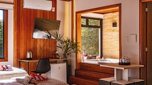 A modern bathroom with a wooden vanity, a large mirror, a sink, and a window with a stone wall view. - Invernada Blessmann  (Vespasiano Corrêa)