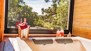 A bathtub with a view of trees through a window, a bucket with a towel, and two bottles on the side. - Invernada Blessmann  (Vespasiano Corrêa)