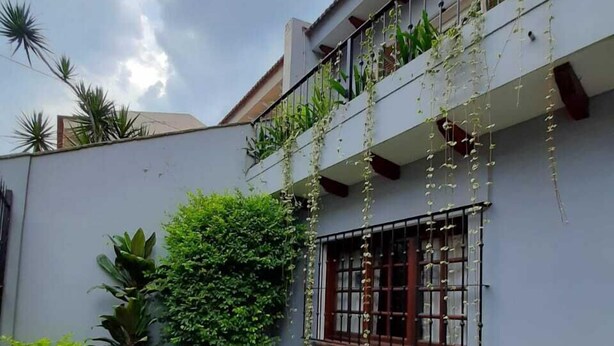 A two-story building with a balcony, surrounded by lush greenery and a well-maintained lawn.