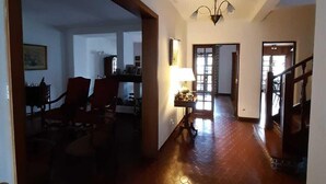 A spacious hallway with a wooden floor, a dining area with chairs and a table, and a staircase leading to another level.