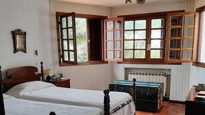 A room with two wooden beds, a ceiling fan, a radiator, and a window with open shutters.
