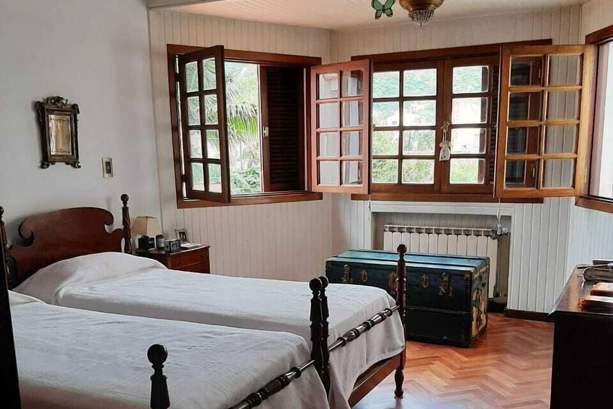 Une chambre avec deux lits en bois, un ventilateur de plafond, un radiateur et une fenêtre dont les volets sont ouverts.