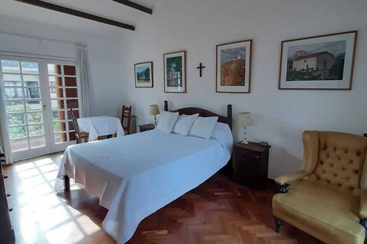 Une chambre à coucher avec un grand lit, une chaise, une table de chevet et une croix accrochée au mur.