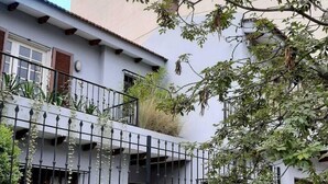 A residential building with a balcony, a metal fence, and a tree.