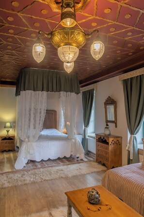 A bedroom with a four-poster bed, a wooden nightstand, a dresser, and a table with a decorative object. - Shamrock Elati Retreats (Zagori)