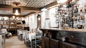 Een restaurant met een bar, houten tafels en stoelen, en diverse flessen en glazen op de planken.