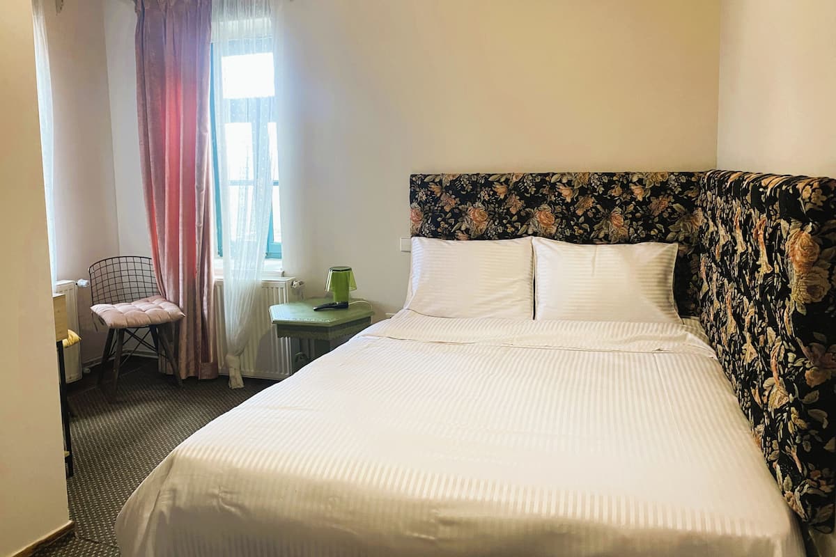 Een hotelkamer met een groot bed, een stoel, een klein tafeltje en een raam met gordijnen.