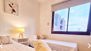 A hotel room with two beds, a nightstand, a lamp, and a window with a city view. - Balcon de Caseros (Salta)