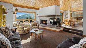 A cozy living room with a fireplace, comfortable seating, and a large window offering a mountain view. - Big Sky Ski in- Ski out retreat/ Freshly Remodeled (Big Sky)