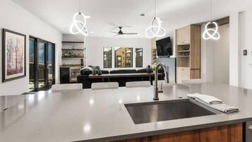 Une cuisine moderne dotée d’un îlot central, de luminaires suspendus et offrant une vue sur l’espace de vie.