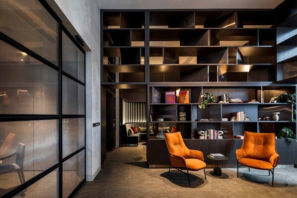 A modern interior with a large bookshelf, two orange armchairs, and a small round table. - Luxury Central CBD Westside Place. Heated Pool, Gym, Sauna, Steam, and more! (Melbourne)