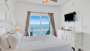 A bedroom with a bed, a television, a dresser, and a view of the ocean. - Beachfront Escape | Pet Friendly | Fort Morgan (Gulf Shores)