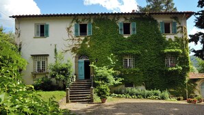 A two-story house with a covered porch, a front door, and a set of stairs leading to the entrance. - The Ancient Farmhouse in Caiano – a dive into history, books, nature. (Toscana)