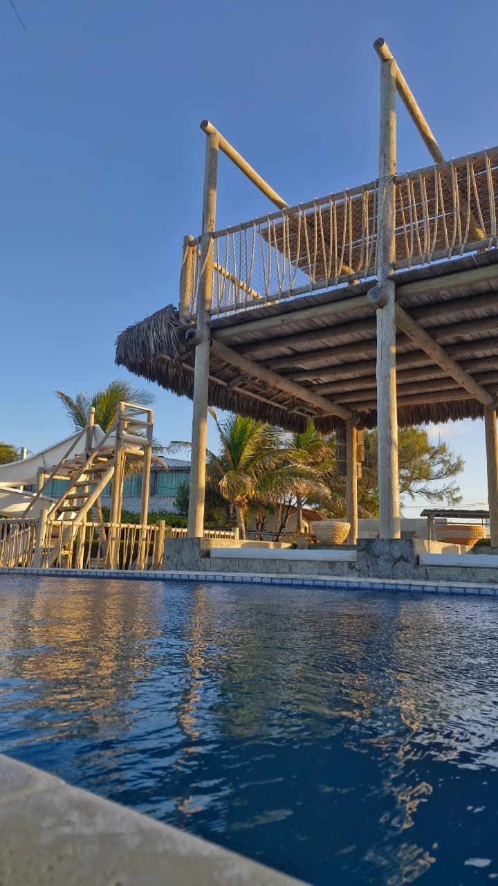 Zona de piscina con un deck de madera y una estructura de techo de paja.
