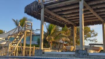 Zona de piscina con un deck de madera y una estructura de techo de paja.