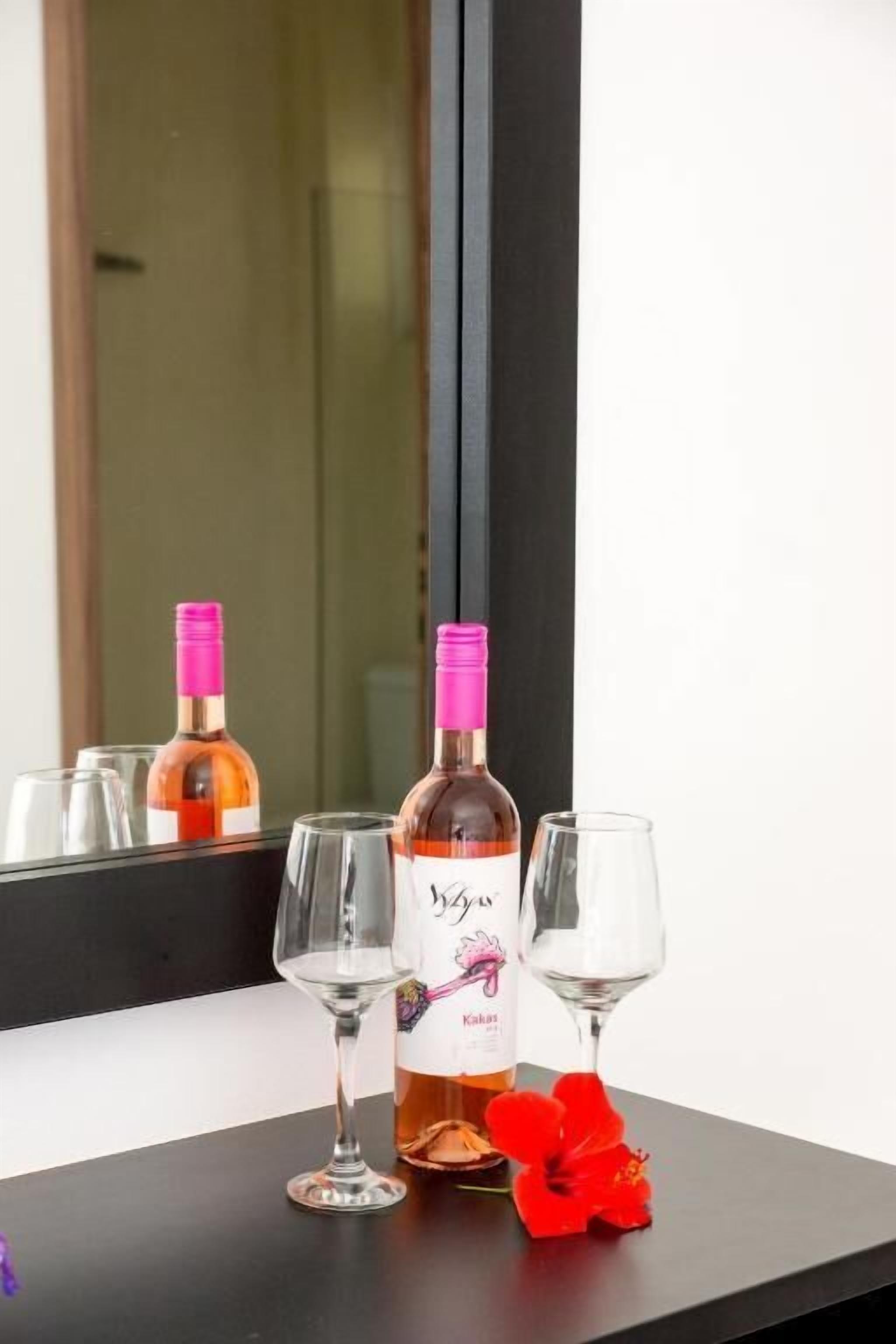 A bottle of wine and two glasses on a black surface with a red flower.