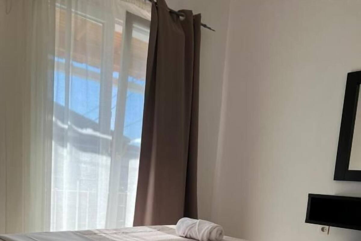 A hotel room with a bed, a TV, and a window with curtains.