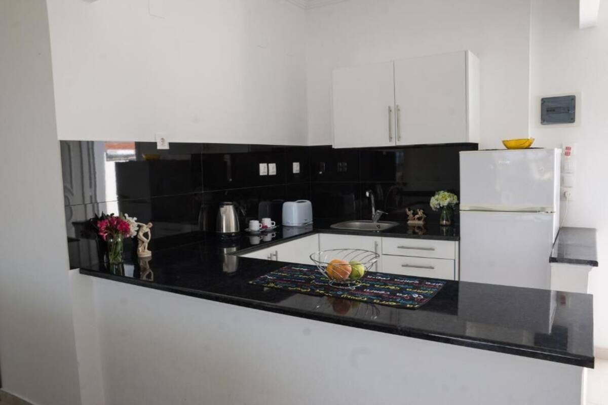 A modern kitchen with black countertops, white cabinets, and a small island with a fruit bowl.