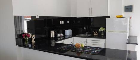 A modern kitchen with black countertops, white cabinets, and a small island with a fruit bowl.
