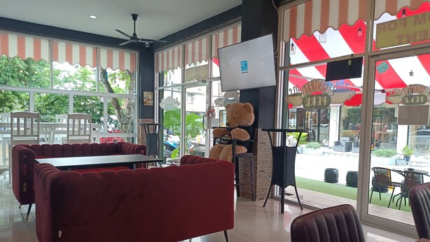 A restaurant interior with red upholstered booths, a large teddy bear decoration, and a view of the street outside. - Central Perk Hotel (Patong)