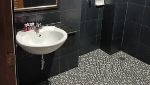 A bathroom with a white sink, a mirror, a shower, and a tiled floor. - Central Perk Hotel (Patong)
