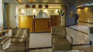 A hotel lobby with a reception desk, two leather chairs, a marble table, and a potted plant. - The Grand Plaza Hotel (Kampala)