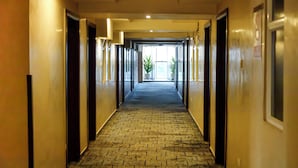 A hotel hallway with a patterned carpet, doors on both sides, and a view into a room with a plant. - The Grand Plaza Hotel (Kampala)