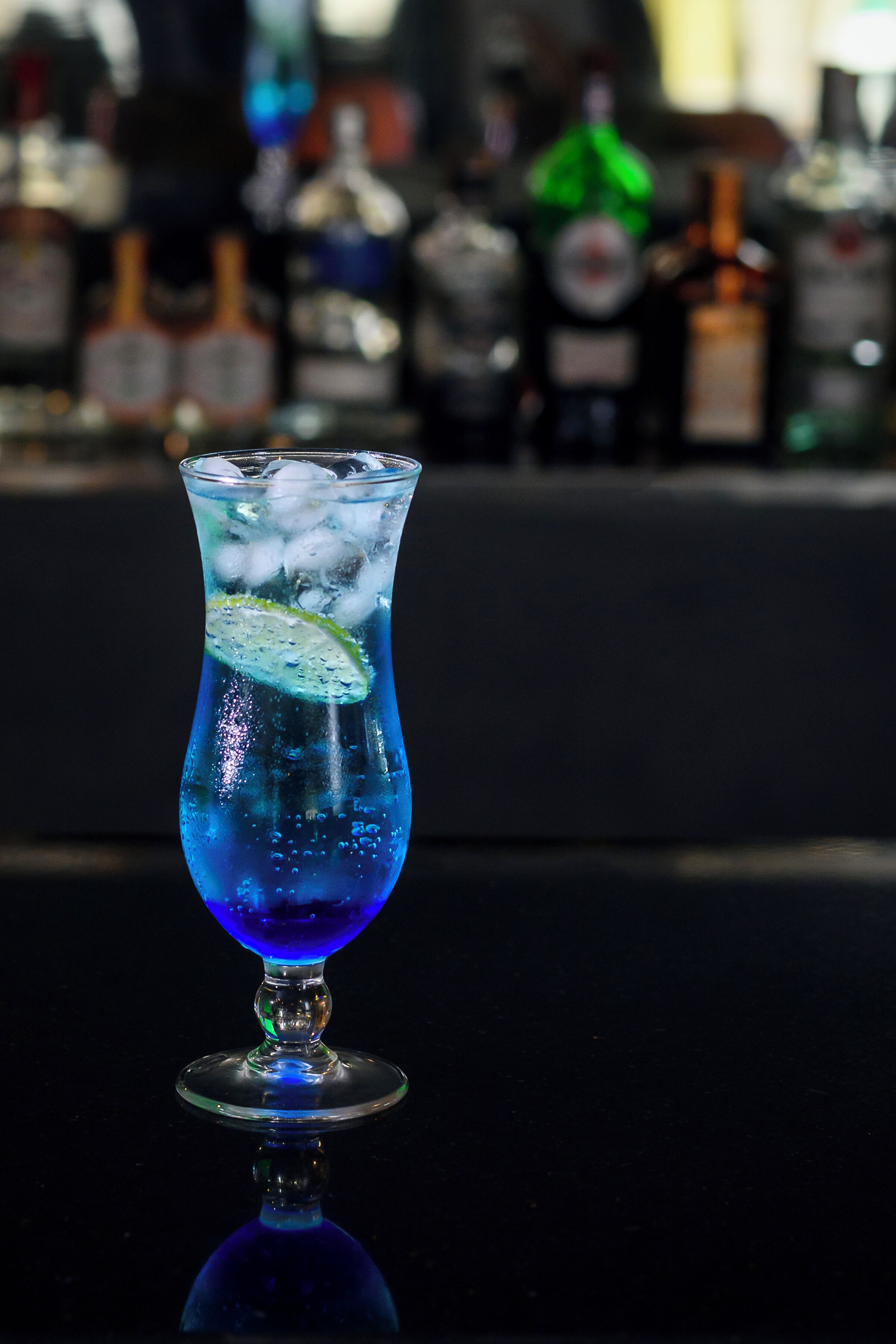 A cocktail glass with ice and a lime slice on a reflective surface.