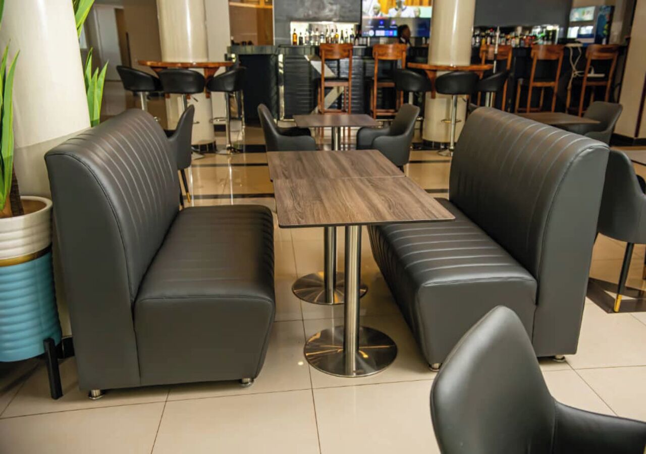 Un espace salon moderne avec des canapés en cuir et une table en bois, entouré de tabourets de bar et d’un comptoir de bar en arrière-plan.