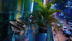 A balcony with wicker chairs and a potted plant, overlooking a busy street. - The Grand Plaza Hotel (Kampala)