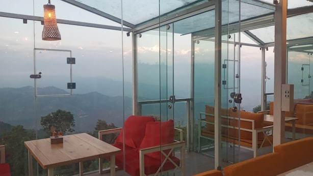 Une pièce fermée par des parois de verre, avec une table en bois et une chaise rouge, d’où l’on peut admirer la vue sur les montagnes lointaines.