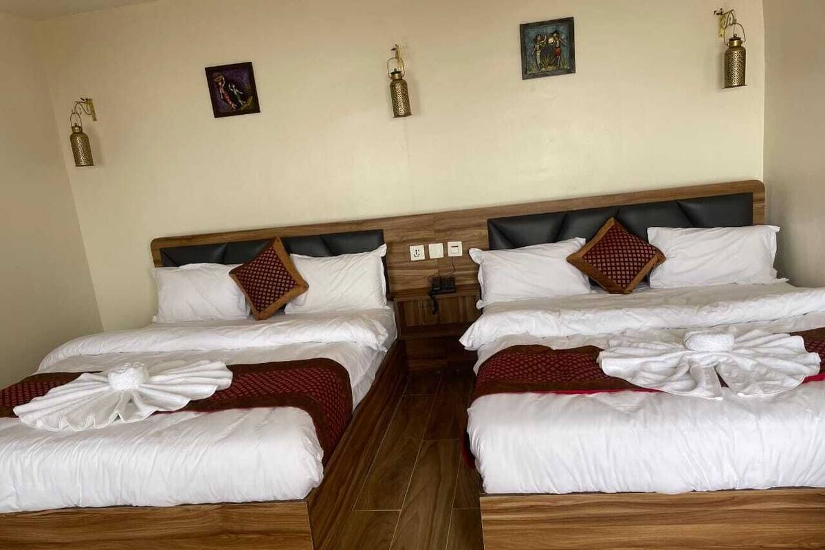 Habitación de hotel con cuatro camas dispuestas en fila, cada una con ropa blanca y detalles en rojo.
