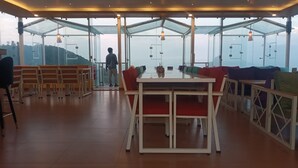 Un espace intérieur vaste, avec une grande table et des chaises, un mur de verre donnant sur l’extérieur, et une personne debout près de ce mur de verre.