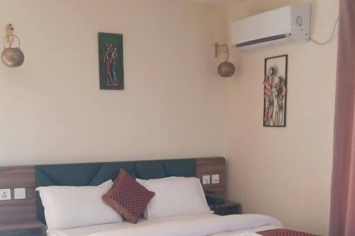 Una habitación de hotel con cama, mesita de noche, aire acondicionado y decoración en la pared.